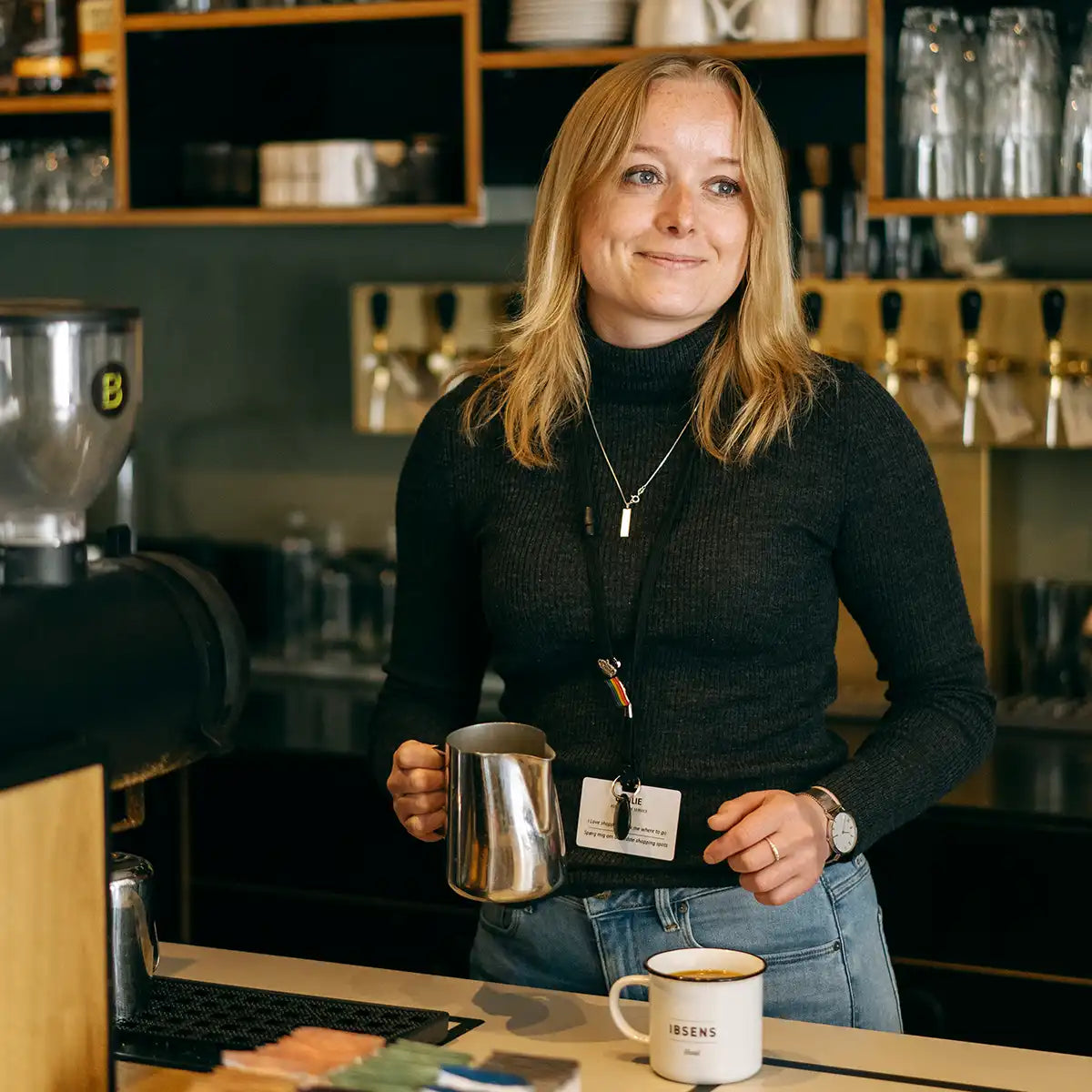 kvinde i kaffebar med mælkekande klar til at lave latteart