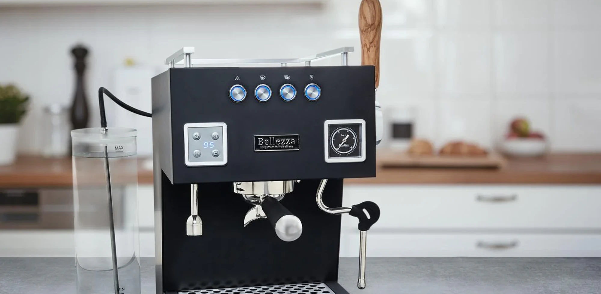 Sort Bellezza espressomaskine med sløret køkkenbaggrund.