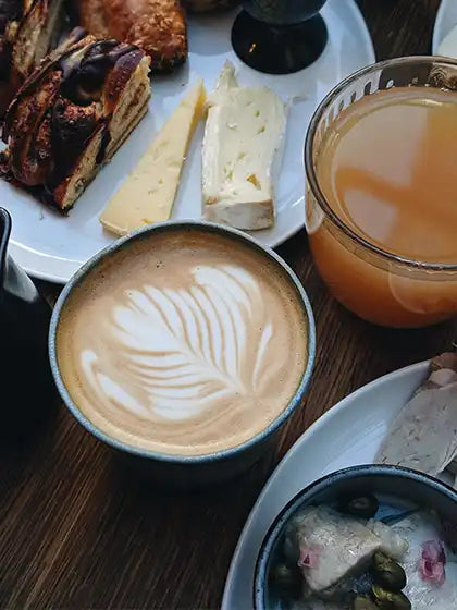 Kaffekop med latteart på bord med assorteret madvarer.