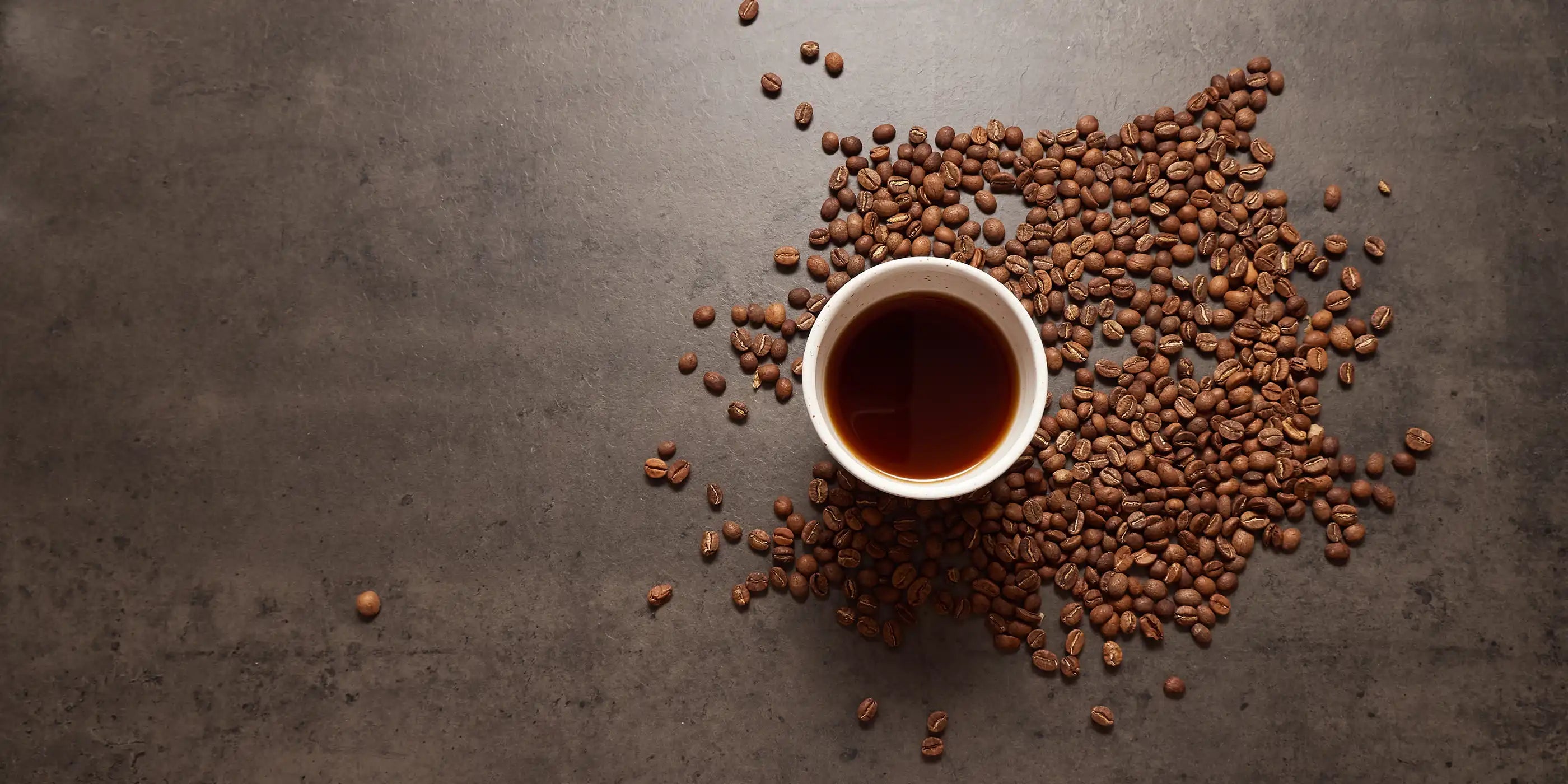 kaffekop med kaffebønner spredt rundt om 