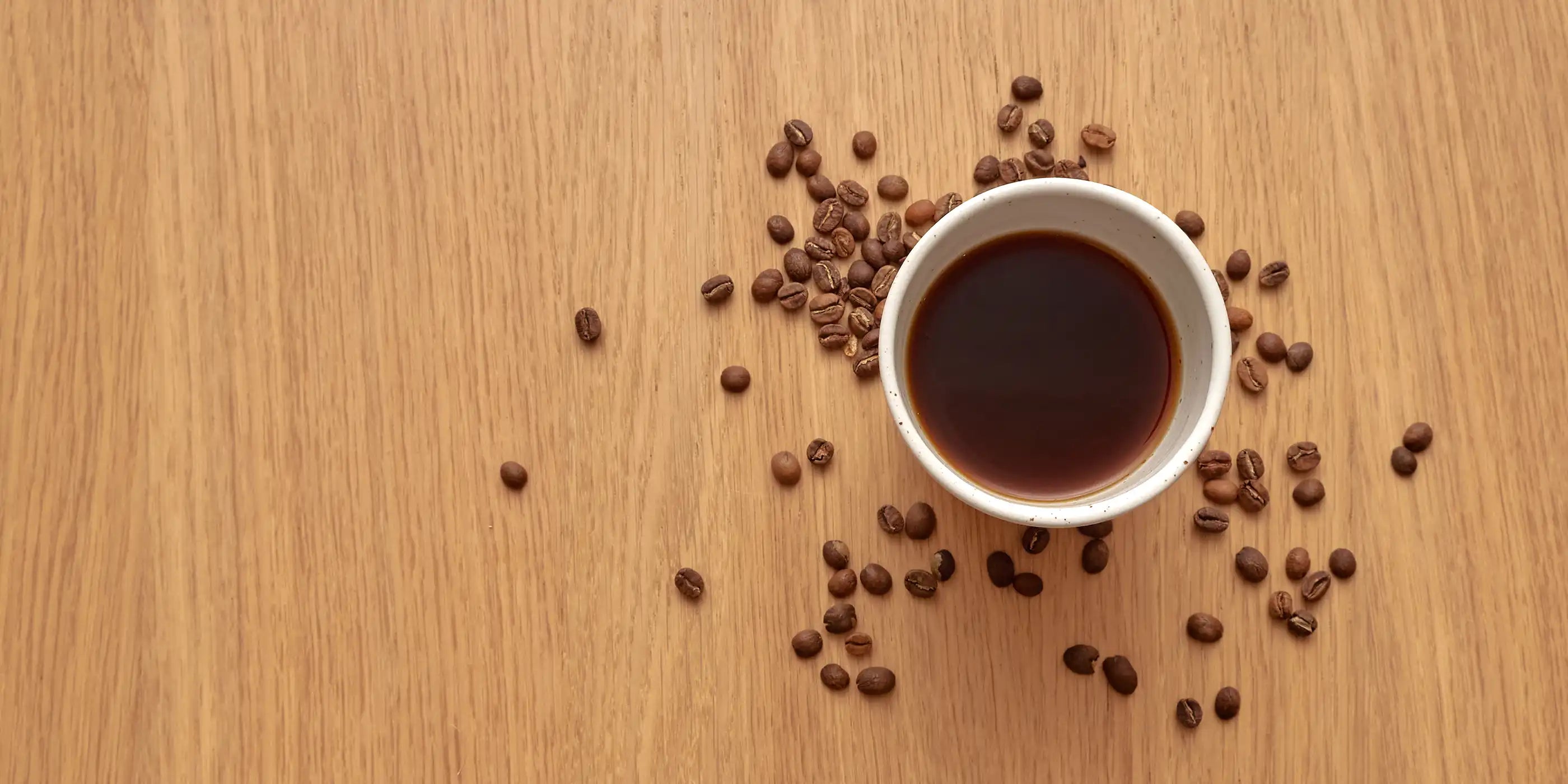 kaffekop på træbord med kaffebønner rundt om 